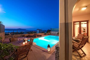 A pool area with a view of the sea, outdoor seating, and a stone wall. - Villa Aphrodite in Plaka (Apokoronas)