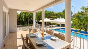 Un espace extérieur abrité, aménagé pour les repas, avec vue sur la piscine, doté de mobilier en osier et de parasols.