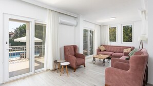 Un salon spacieux doté d’une porte-fenêtre coulissante donnant sur un balcon, d’un canapé rose et d’une petite table ronde.