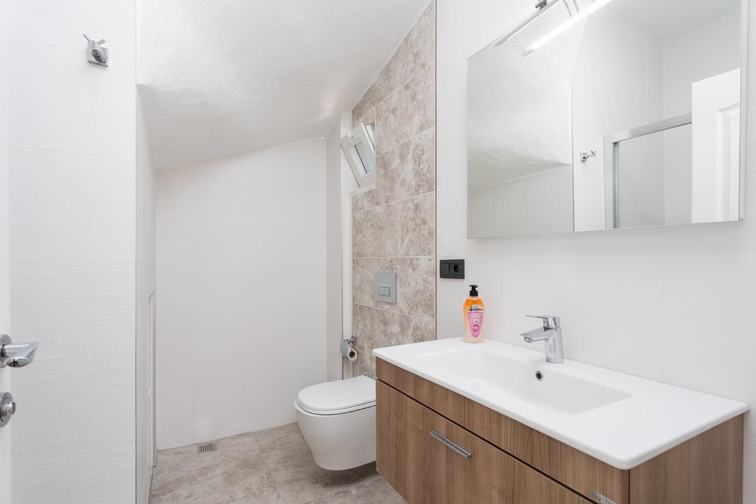 A modern bathroom with a white toilet, a wooden vanity, and a large mirror.