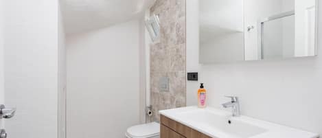 A modern bathroom with a white toilet, a wooden vanity, and a large mirror.