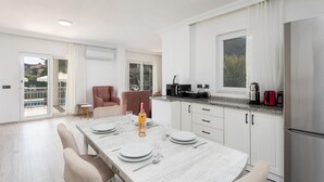 Une cuisine moderne avec des meubles blancs, une table à manger pour quatre personnes et une grande fenêtre.