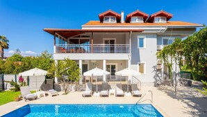Une maison à deux étages avec une piscine, un espace salon extérieur et un jardin clôturé.