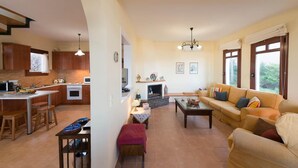 A modern kitchen with a dining area, a living room with a sofa and coffee table, and a fireplace. - Ariadne Villa in Plaka (Apokoronas)