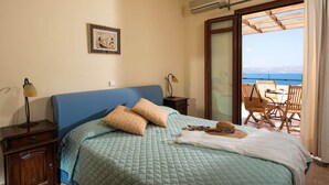 A bedroom with a bed, bedside tables, a picture on the wall, and a view of the sea through a sliding glass door. - Ariadne Villa in Plaka (Apokoronas)