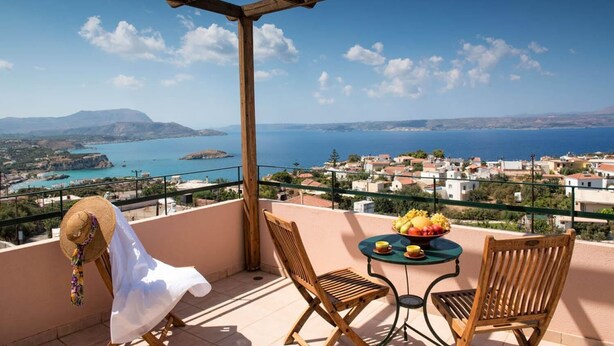 A balcony with a wooden pergola, two wooden chairs, a small round table with a bowl of fruit, and a straw hat on the left. - Ariadne Villa in Plaka (Apokoronas)