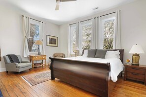 A bedroom with a wooden bed, a chair, a nightstand, and a window with blinds.