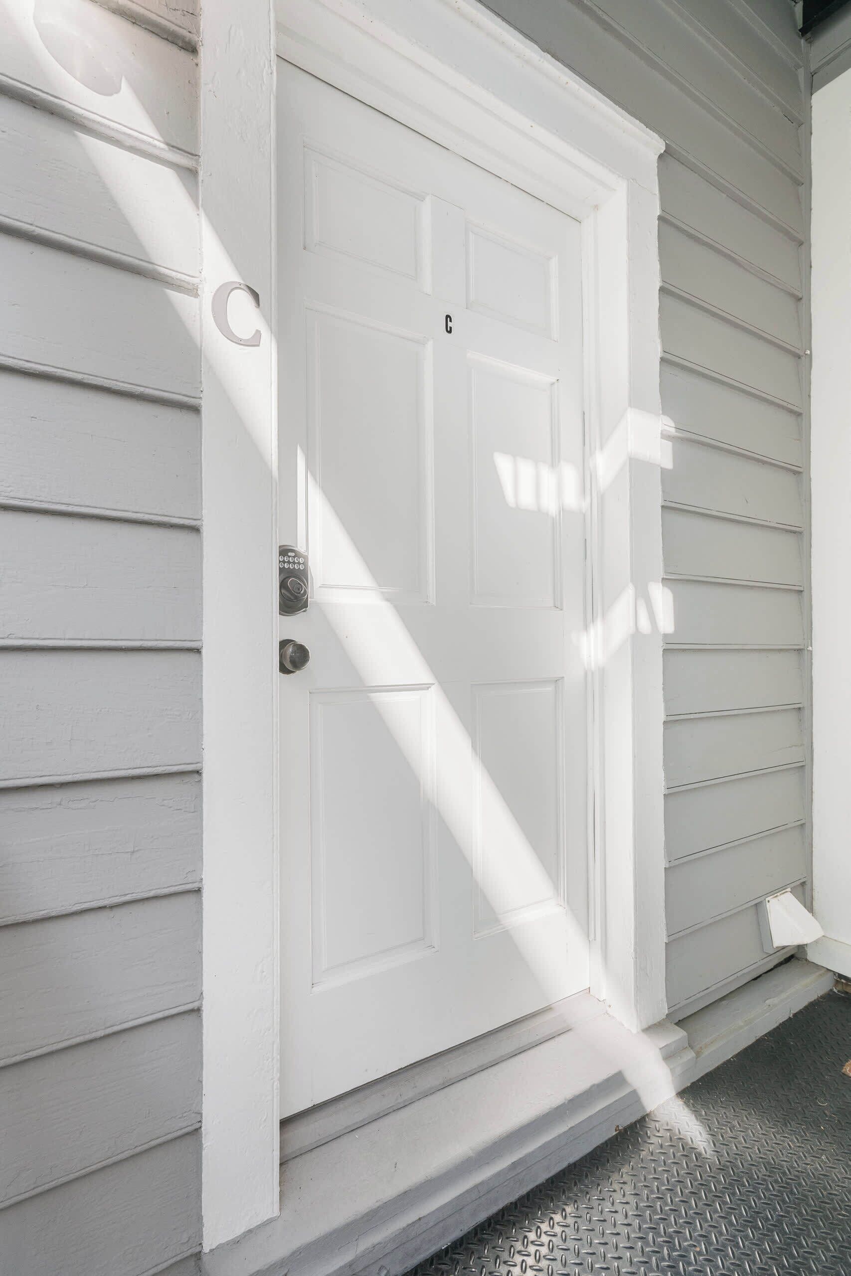 A white door with a keypad lock, set in a white exterior wall with horizontal siding.