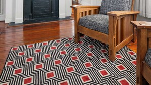 Una sala de estar con chimenea, televisor montado encima y una alfombra estampada en el suelo.