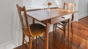 Un comedor con una mesa y sillas de madera, una ventana con cortinas translúcidas y una obra de arte enmarcada en la pared.