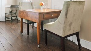 A dining area with a wooden table, two chairs, a vase with flowers, and a window with a view of trees. - The Retreat | Downtown King 2BD w/ Porch + Parking (Charleston)