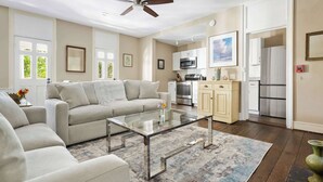 A spacious living room with a glass coffee table, beige sofas, and a ceiling fan. - The Retreat | Downtown King 2BD w/ Porch + Parking (Charleston)