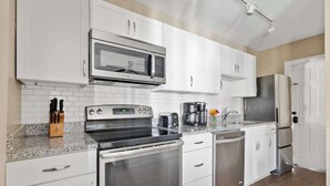 A modern kitchen with white cabinetry, stainless steel appliances, and granite countertops. - The Retreat | Downtown King 2BD w/ Porch + Parking (Charleston)