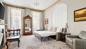 Un dormitorio amplio con una cama grande, un área de descanso con un sofá y sillones, una mesa de madera y un espejo grande.