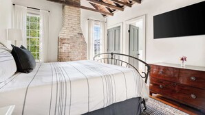 Een slaapkamer met een bed, een dressoir, een televisie en een bakstenen muur.