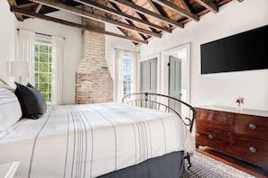 A bedroom with a bed, a dresser, a TV, and a brick wall. - Historical 2bd Home w. Outdoor Space + Parking (Charleston)