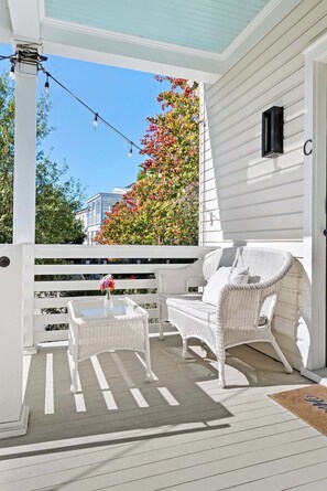 A covered porch with white wicker furniture, a small table with a vase, and a mailbox on the wall.