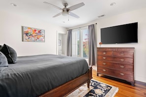 A bedroom with a bed, a dresser, a ceiling fan, a TV, and a window with curtains.