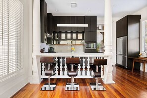 A modern kitchen with dark cabinetry, a white island with bar stools, and stainless steel appliances. - Historical 2bd Home w. Outdoor Space + Parking (Charleston)