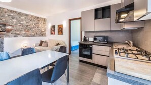 Una cucina compatta con elettrodomestici moderni, un'area pranzo con tavolo bianco e sedie blu, e una parete decorativa in pietra.