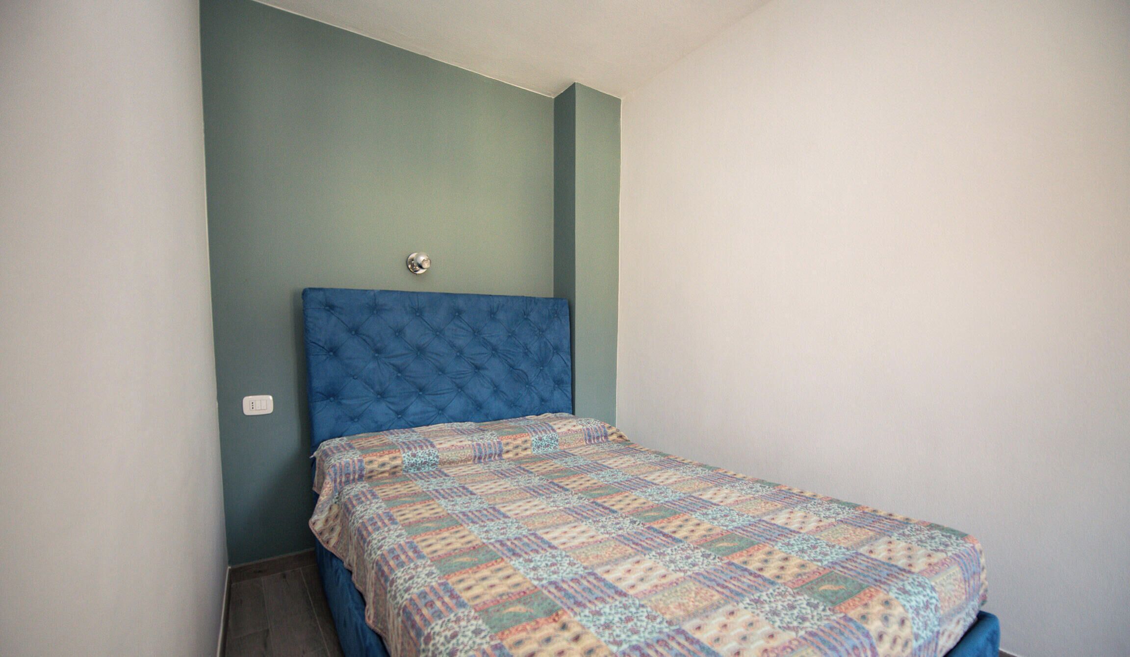 Une chambre à coucher avec une tête de lit bleue, une couvre-lit à motifs et une petite table de chevet.