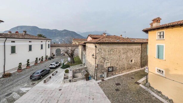 A narrow street with traditional stone buildings, a paved road, and parked cars. - Secret Garda (San Felice del Benaco)