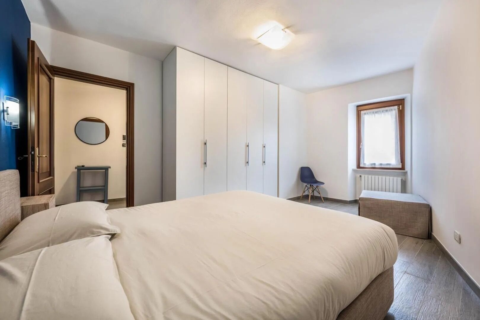 Een slaapkamer met een bed, kledingkast, nachtkastje, stoel en een raam.