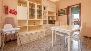 A room with a dining table, chairs, a white cabinet with glass doors, a red first aid kit, and a window with a view. - Attico Vintage Colette by Rentbeat (Verona)