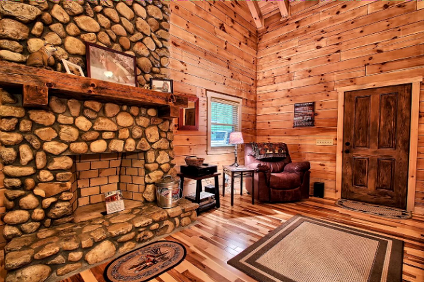 A log cabin interior with a stone fireplace, wooden walls, a leather chair, and a wooden door.