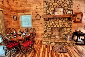 A rustic cabin interior with a stone fireplace, wooden dining table, and chairs. - Large Log Cabin Rental Perfect for Families in Hocking Hills, Ohio (Logan)