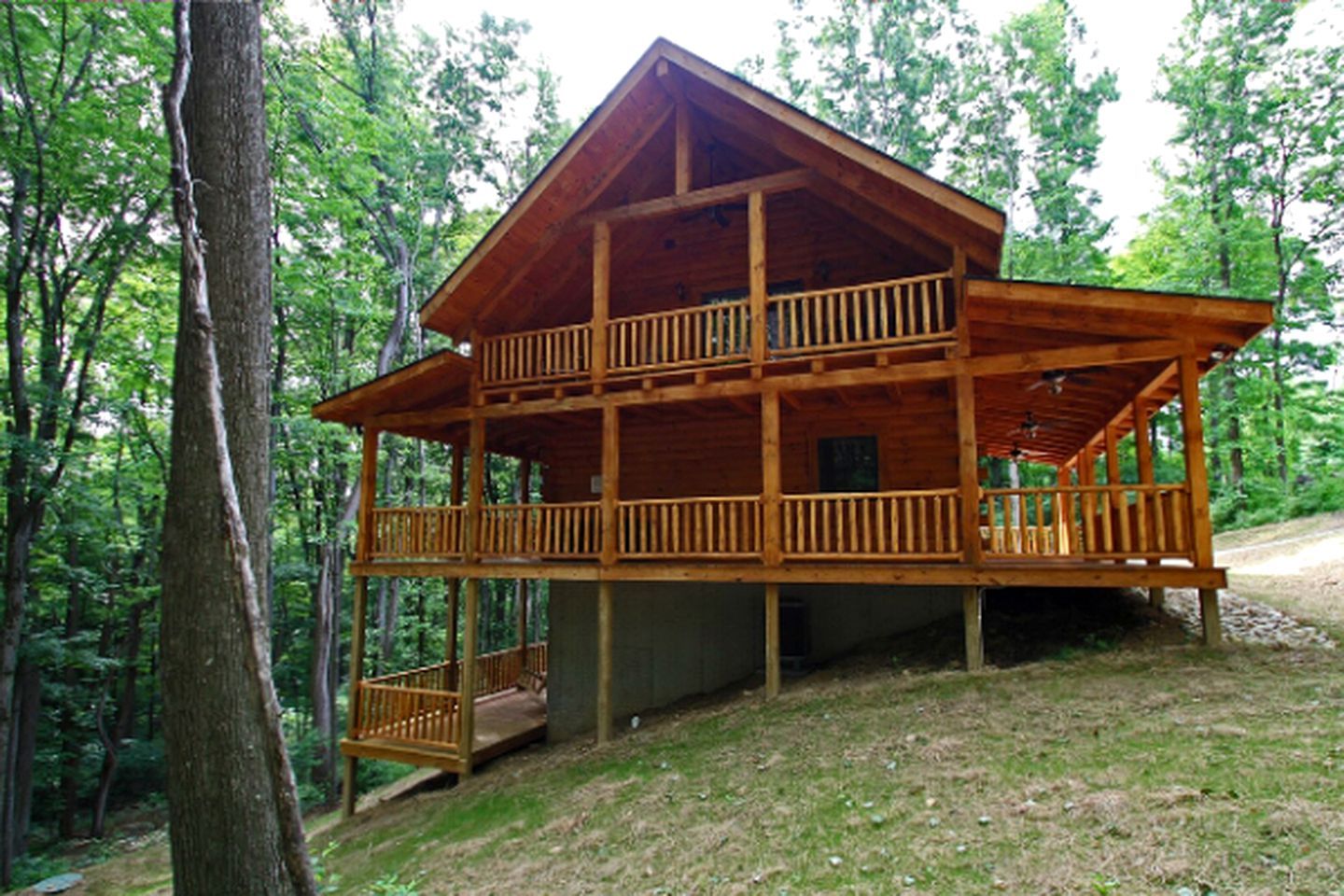 A two-story wooden cabin with a balcony on the upper floor, surrounded by trees.