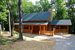 A cabin with a porch, a chimney, and a gravel driveway surrounded by trees. - Large Log Cabin Rental Perfect for Families in Hocking Hills, Ohio (Logan)