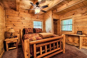 A wooden cabin room with a bed, a ceiling fan, a nightstand, and a window. - Large Log Cabin Rental Perfect for Families in Hocking Hills, Ohio (Logan)