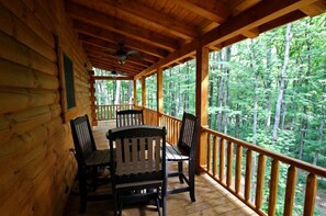 A wooden cabin with a covered porch, a table with chairs, and a view of a forest. - Large Log Cabin Rental Perfect for Families in Hocking Hills, Ohio (Logan)