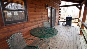Una baita di legno con un portico coperto, un tavolo in metallo con sedie e un barbecue.