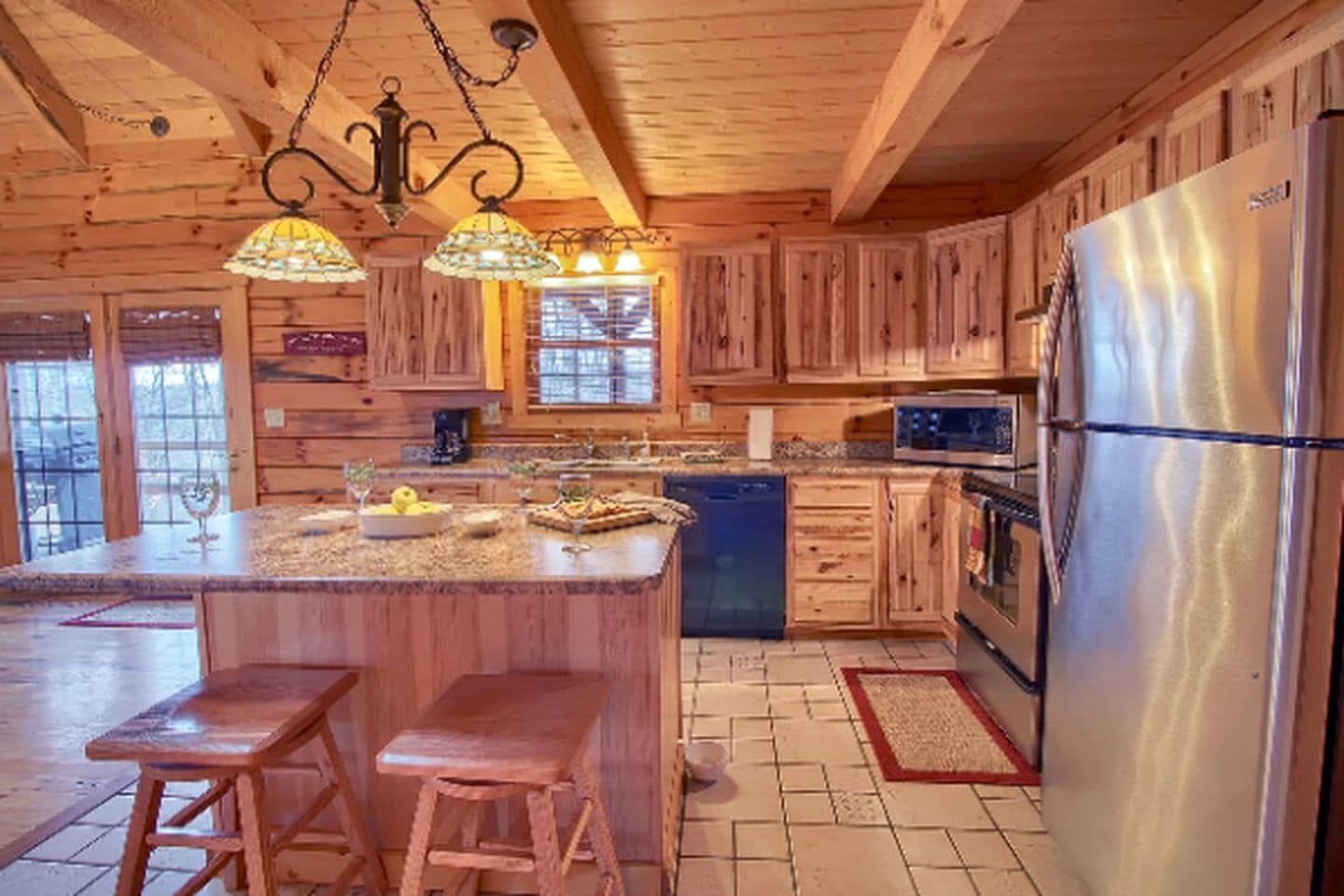 A wooden cabin-style kitchen with a central island, bar stools, a refrigerator, and a dishwasher.