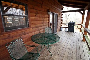 A wooden cabin with a covered porch, a metal table with chairs, and a grill. - Secluded Log Cabin Rental with a Hot Tub in the Hocking Hills, Ohio (Logan)