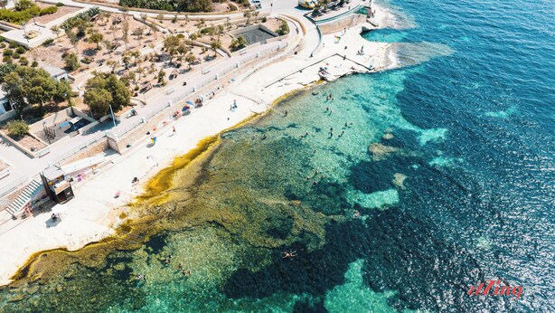 Vista aèria d'una zona costanera amb una platja, aigua cristal·lina i un passeig marítim.