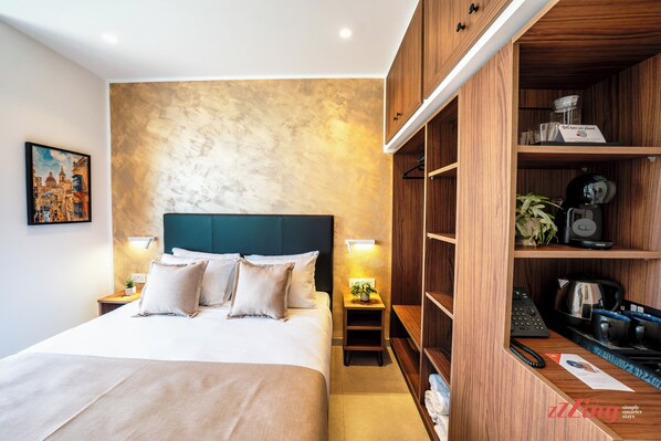 A modern hotel room with a large bed, wooden wardrobe, and a small side table with a plant.