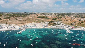 Vista aèria d'una població costanera amb un port ple de vaixells, una platja sorrenca i edificis al passeig marítim.