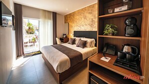 Habitació d'hotel moderna amb un llit gran, una taula de treball amb un fabricant de cafè, un telèfon i una estant amb una planta i un got.