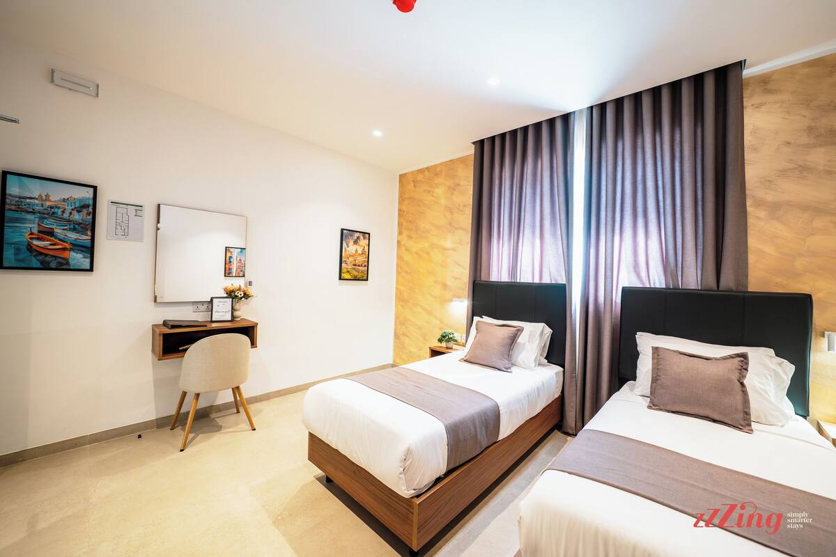 A hotel room with two beds, a desk, and a chair.