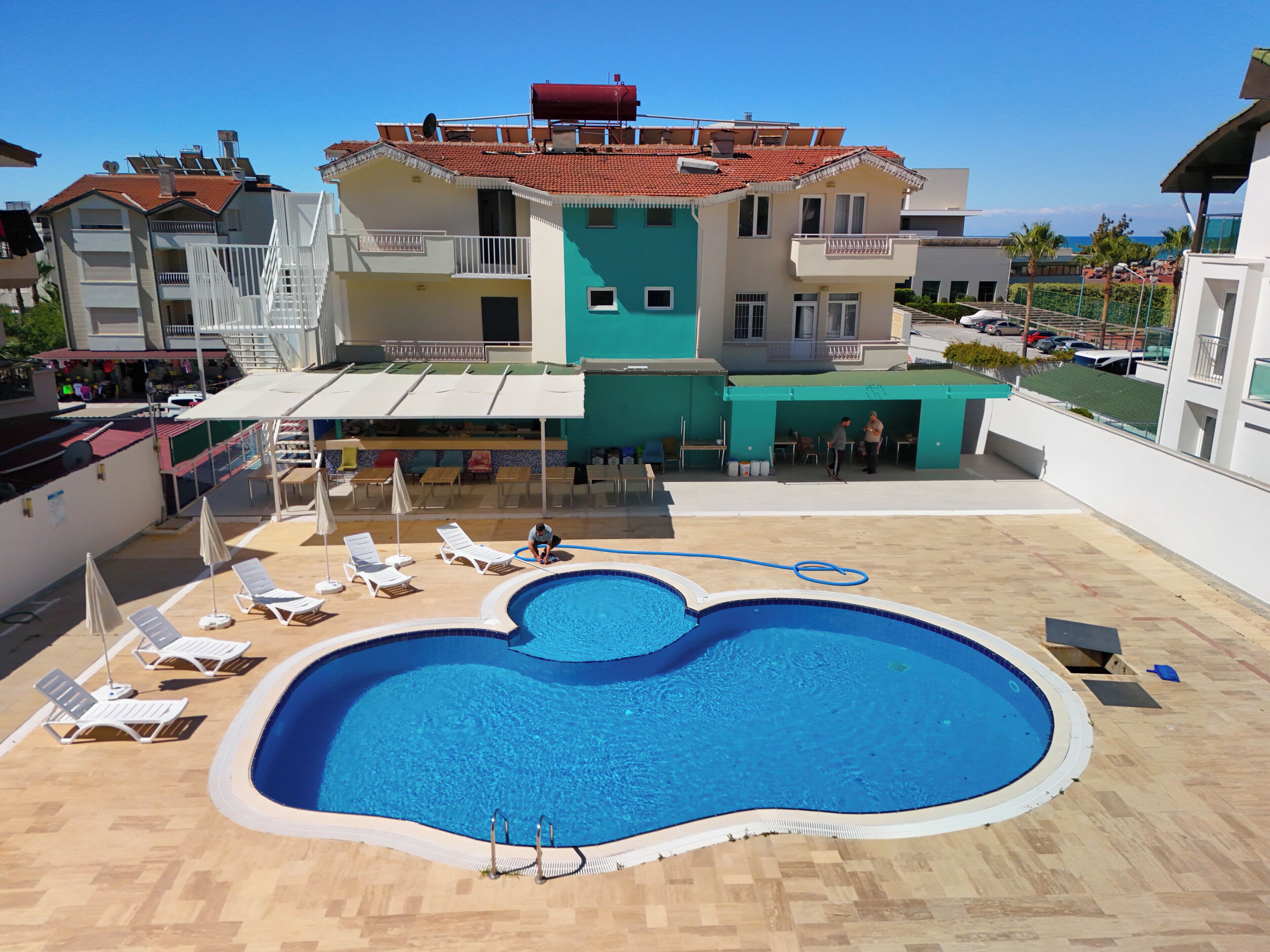 A rooftop pool with lounge chairs, a building with balconies, and a clear blue sky.