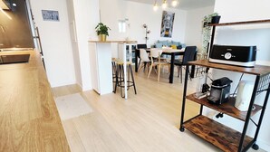 Una cocina moderna con horno empotrado, una zona de comedor con mesa y sillas de madera, y una cafetera en un estante.