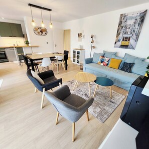 Ein modernes Wohnzimmer mit Sofa, Sesseln, einem Couchtisch und einem Essbereich mit Tisch und Stühlen.