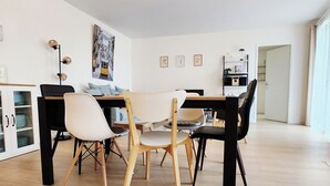 Un comedor moderno con una mesa de madera, sillas negras y un sofá blanco. Hay tres lámparas colgantes sobre la mesa.