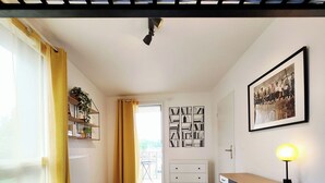 Una cocina luminosa y moderna con piso de madera, un armario blanco, una mesa de comedor con dos sillas y una lámpara colgante.