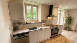 Een moderne keuken met witte kasten, een roestvrijstalen vaatwasser, een gasfornuis en een raam met uitzicht op groen.