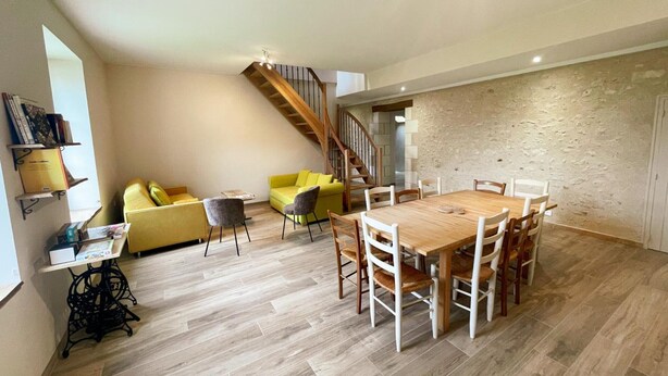 Een ruime woonkamer met een houten eettafel, een gele bank en een trap naar een hoger gelegen verdieping.