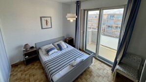 Een slaapkamer met een bed, nachtkastjes, een lamp, een schilderij aan de muur en uitzicht door een groot raam.